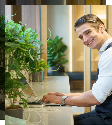 A young man is smiling at the camera while working on his laptop in the adult lounge.