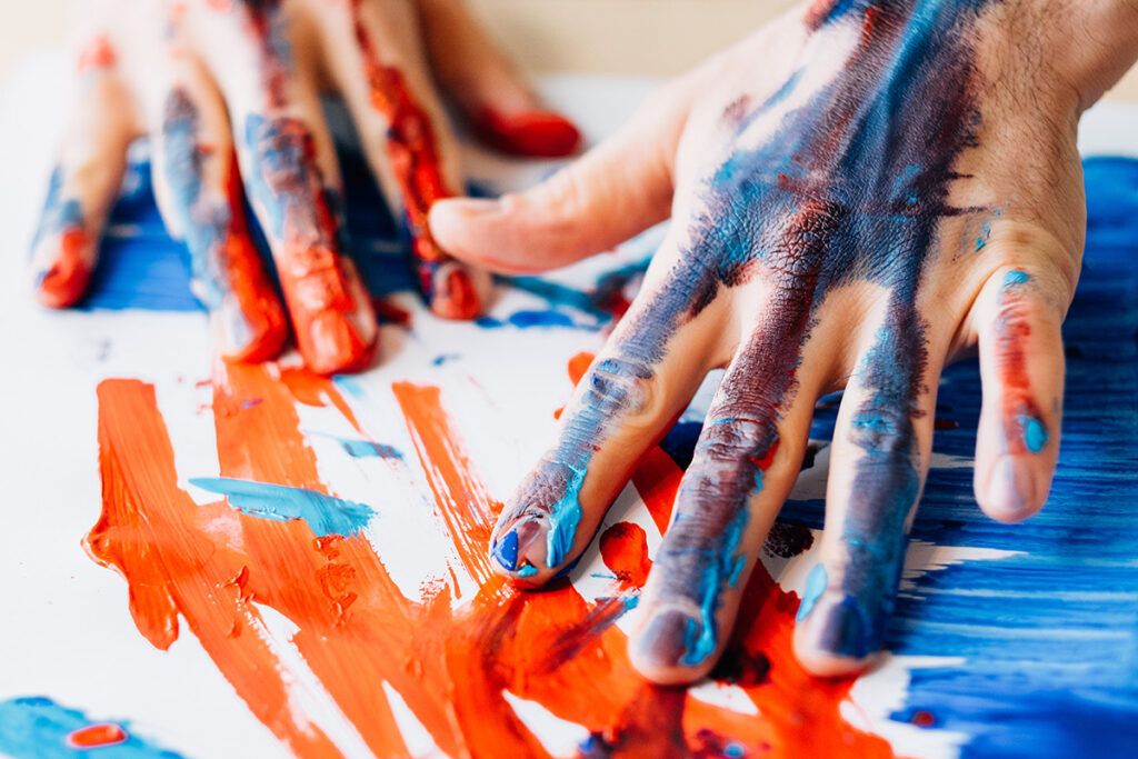 A person with orange and blue paint all over their hands is creating a work of art. It's part of art therapy.