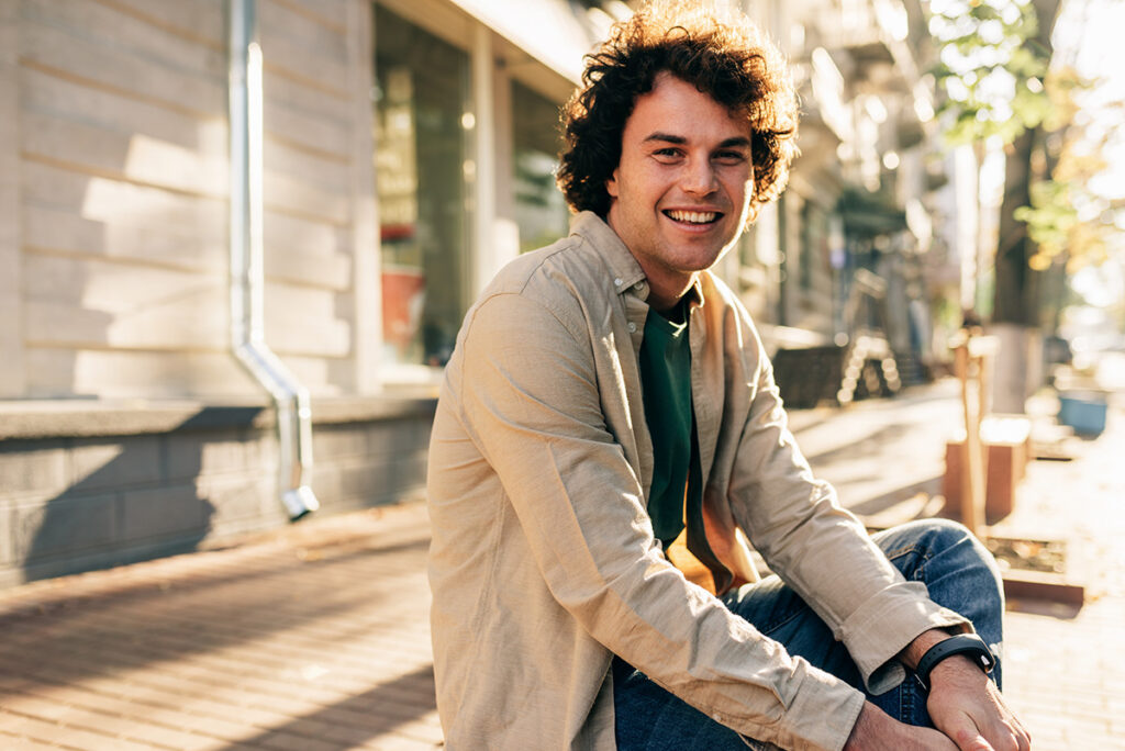 A man is sitting outside and smiling at the camera.