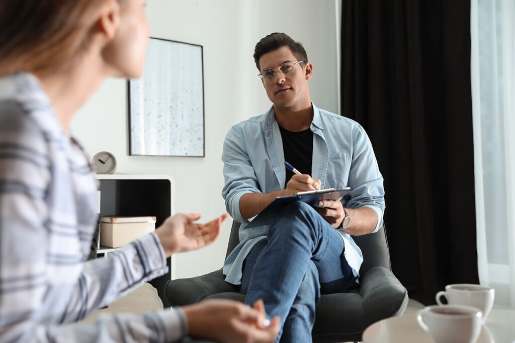 A therapist is taking notes while speaking to a client.
