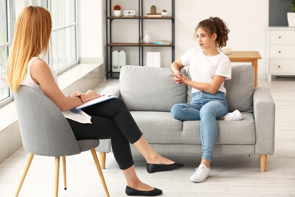 a young woman is sitting on a couch, across from her therapist.