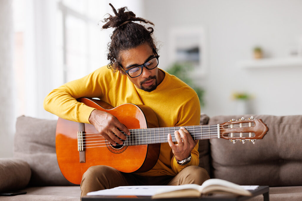 A man is playing his guitar. He is participating in music therapy.