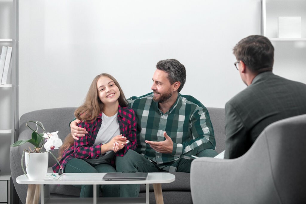 A father and his teen daughter are in family counseling together and smiling.