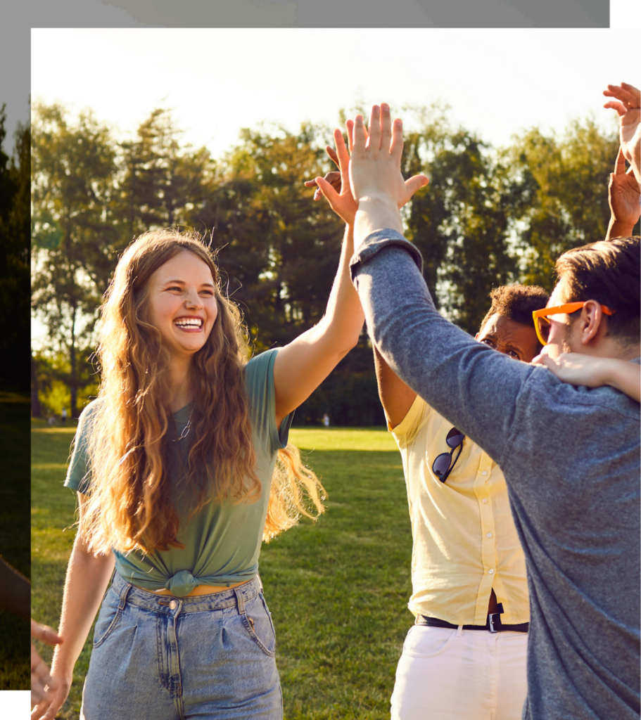 A small group of young people are high-fiving while standing outside in the sunshine. It looks to be in the evening around sunset.