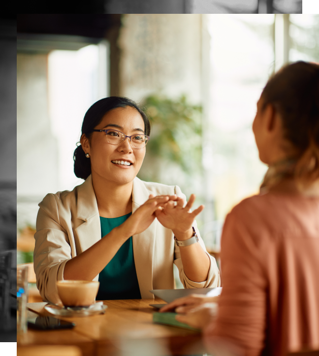 Two women are having coffee together. Light is shining through the window next to them.